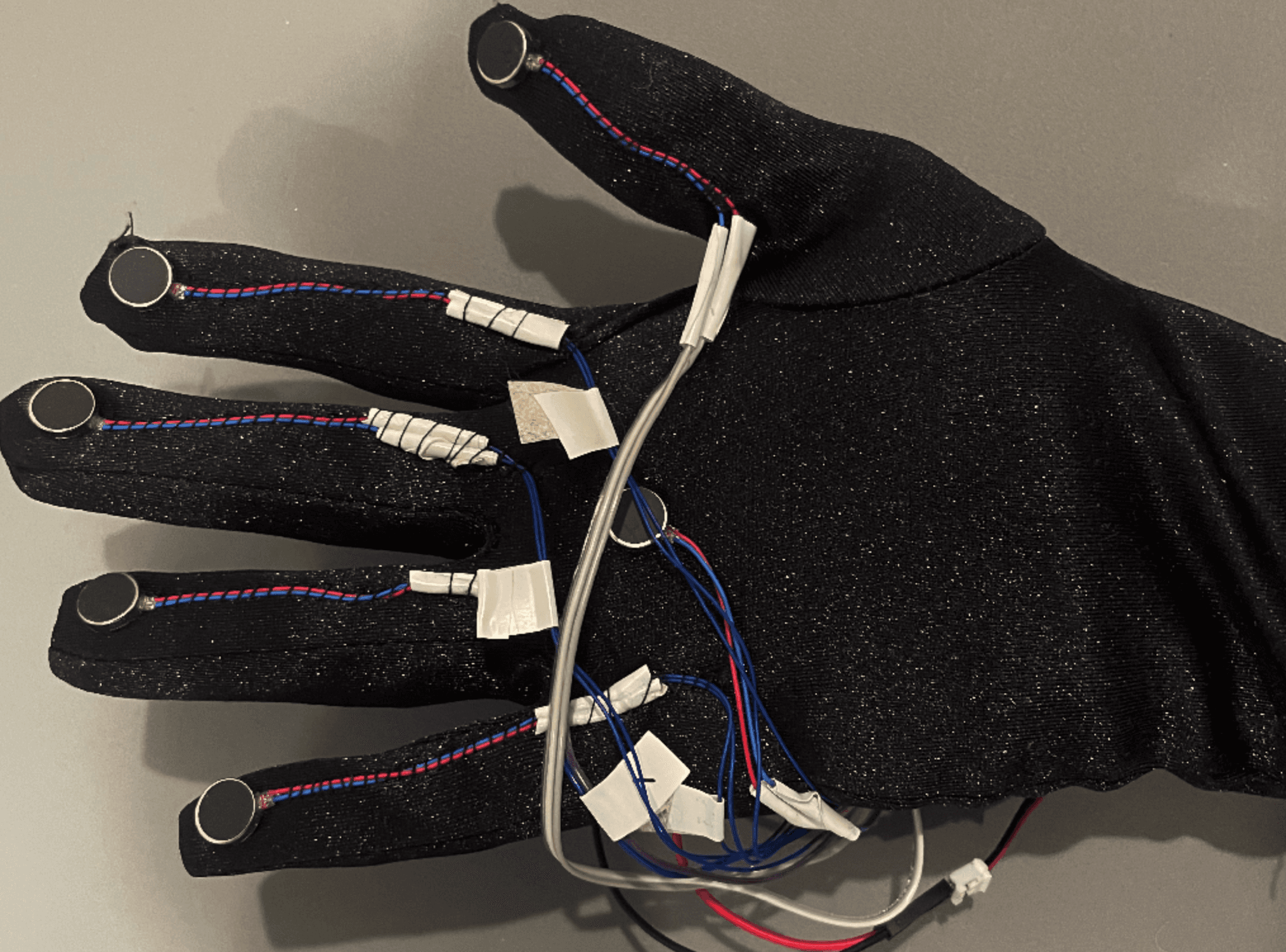 The glove used in the project. Its a black glove with haptic feedback sensors at the fingertips with wires running up to a microcontroller at the wrist.